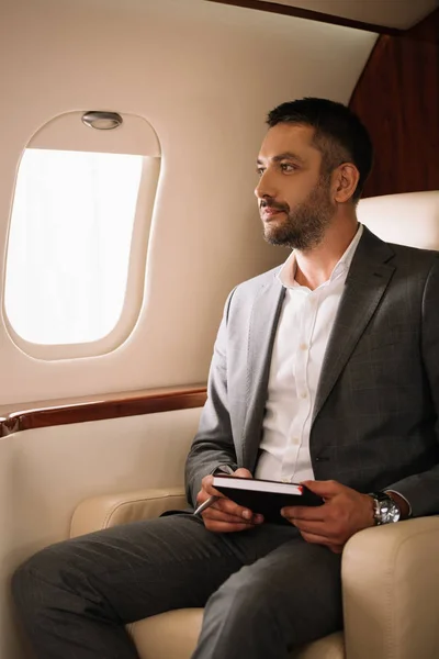 Guapo barbudo hombre de negocios sosteniendo portátil y pluma en jet privado — Stock Photo