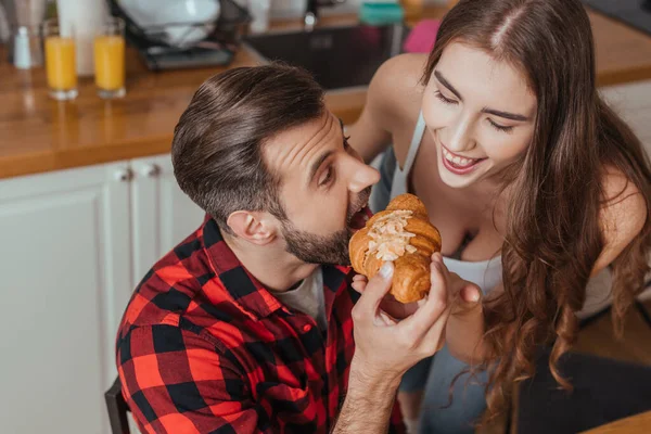Hochwinkel-Ansicht des fröhlichen Mannes, der Croissant in der Nähe einer glücklichen Freundin probiert — Stockfoto
