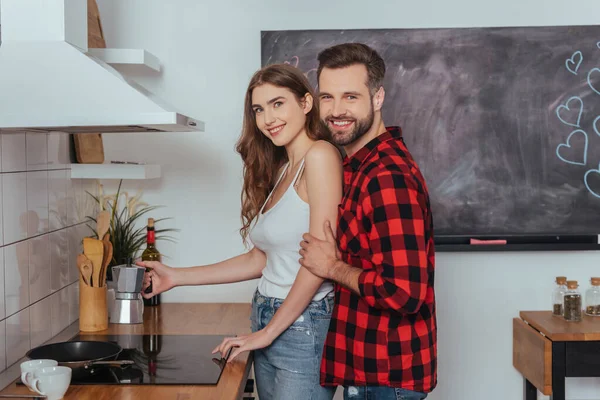 Счастливая молодая пара улыбается в камеру, делая кофе в гейзер кофеварка — стоковое фото