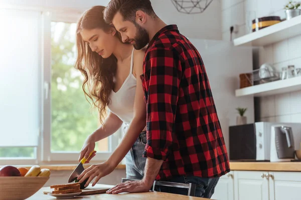 Belle fille coupe fruits frais pour le petit déjeuner près beau petit ami — Photo de stock