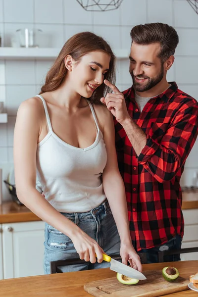 Homme joyeux toucher le nez de petite amie heureuse couper avocat frais — Photo de stock