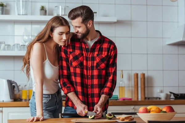 Beautiful girl leaning on shoulder of handsome boyfriend cutting fresh avocado — Stock Photo