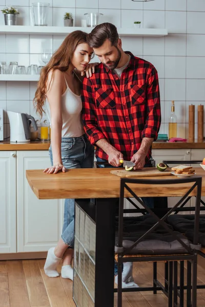 Attraktives Mädchen lehnt sich an Schulter eines hübschen Freundes und schneidet frische Avocado — Stockfoto