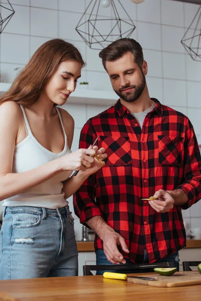 Красивый мужчина смотрит на красивую девушку, режущую свежий авокадо на завтрак — стоковое фото