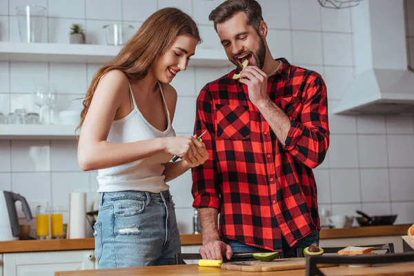 Glücklich schöner Mann Verkostung Scheibe frischer Avocado in der Nähe schöne Freundin Schneiden von Früchten — Stockfoto