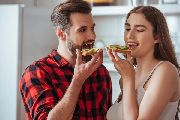 Cheerful young couple holding toasts with fresh avocado — Stock Photo