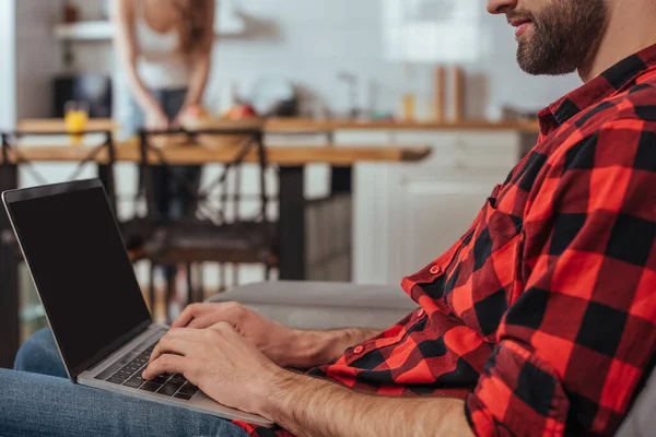 Corte vista de freelancer digitação no laptop com tela em branco na cozinha perto da namorada no fundo — Fotografia de Stock
