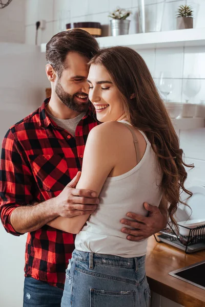 Feliz jovem casal abraçando e sorrindo na cozinha — Fotografia de Stock