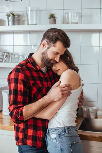 Glückliches junges Paar, das sich mit geschlossenen Augen in der Küche umarmt — Stockfoto