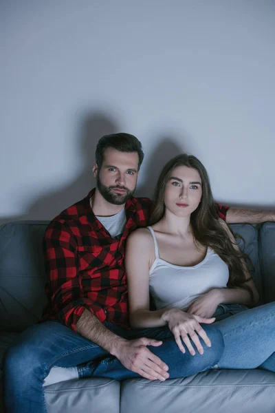 Young, attentive couple watching tv on sofa at home — Stock Photo