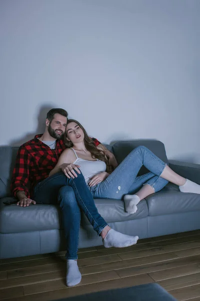 Giovane coppia sorridente guardando la tv sul divano di casa — Foto stock