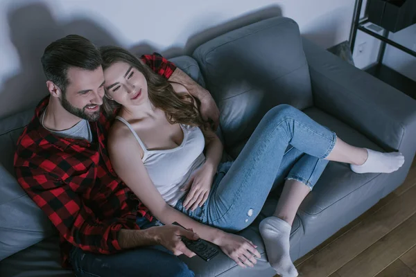 Vue aérienne du couple souriant regardant la télévision sur le canapé à la maison — Photo de stock