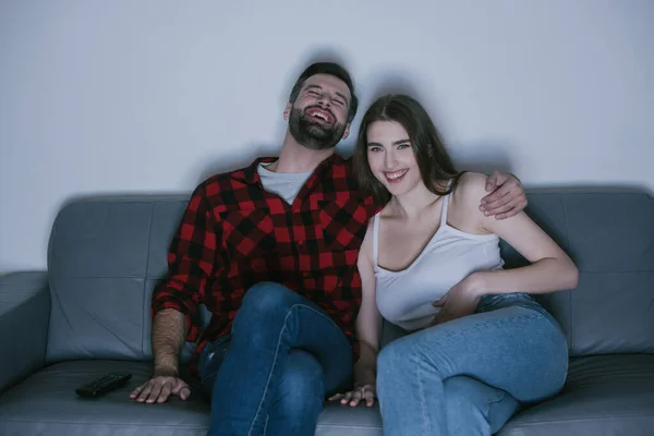 Young couple laughing while watching tv on sofa at home — Stock Photo