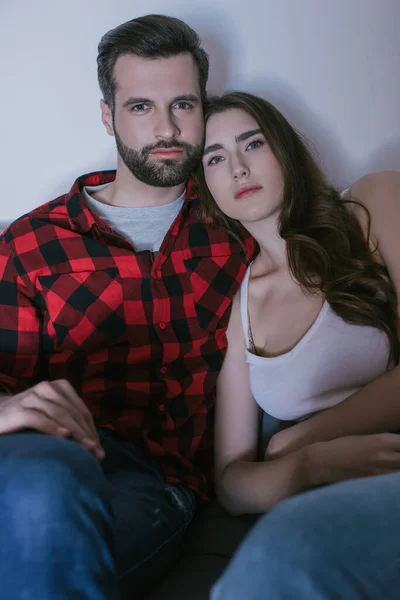 Seria, pareja joven y atenta viendo la televisión en casa - foto de stock