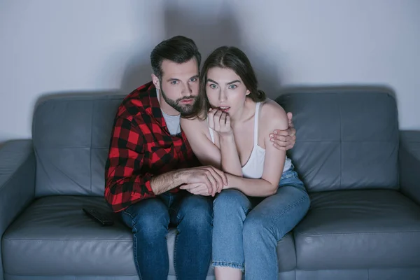 Besorgtes Paar hält Händchen, während es sich zu Hause gemeinsam einen Film ansieht — Stockfoto