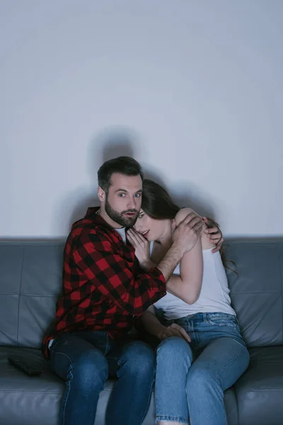 Наляканий чоловік обіймає налякану дівчину, дивлячись фільм разом вдома — стокове фото