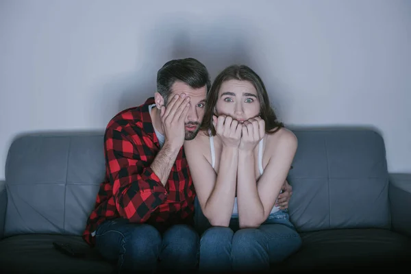 Scared man covering eye with hand while watching movie near frightened girl — Stock Photo