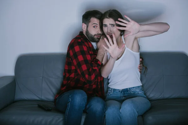 Frightened girl with outstretched hands watching movie near scared boyfriend — Stock Photo