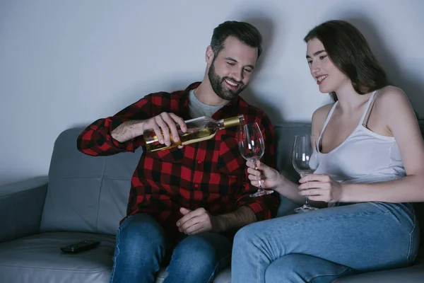 Uomo sorridente versando vino bianco in vetro vicino fidanzata felice — Stock Photo