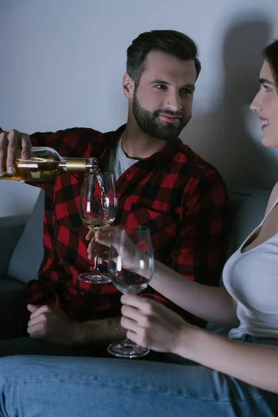 Homem bonito derramando vinho branco em vidro perto da namorada feliz — Fotografia de Stock