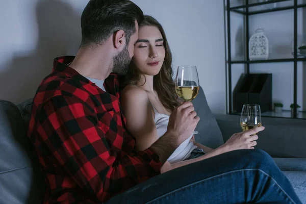 Menina feliz com os olhos fechados sentado no sofá perto namorado com copos de vinho branco — Fotografia de Stock