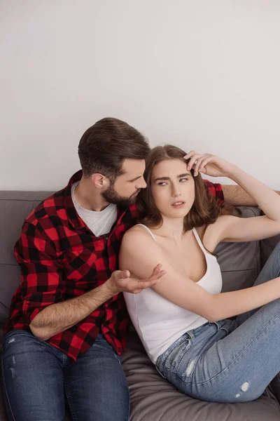 Young man showing shrug gesture while sitting on sofa near depressed girl — Stock Photo