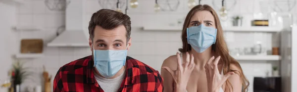 Panoramic shot of angry couple in medical masks screaming while looking at camera — Stock Photo