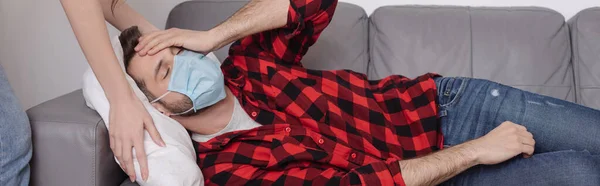 Recortado vista de la mujer tocando almohada mientras enfermo novio acostado en sofá y sosteniendo la mano en la cabeza - foto de stock