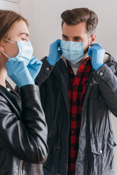 Young couple in latex gloves putting on protective masks before leaving home — Stock Photo