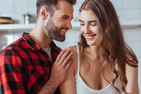 Smiling man touching shoulder of happy young girlfriend in kitchen — Stock Photo