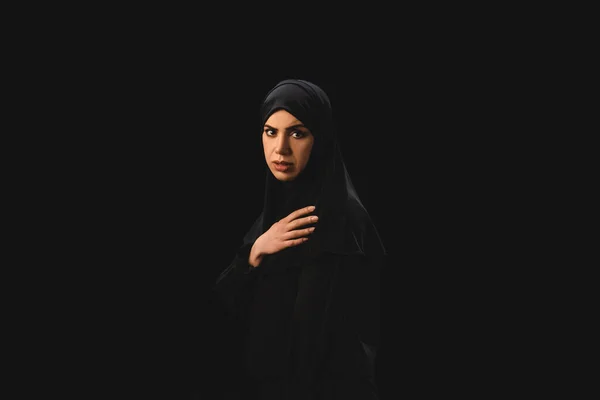 Side view of muslim woman looking at camera isolated on black — Stock Photo