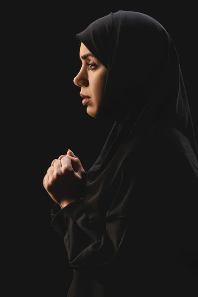 Vista lateral de refugiado musulmán en hijab mirando hacia otro lado aislado en negro - foto de stock