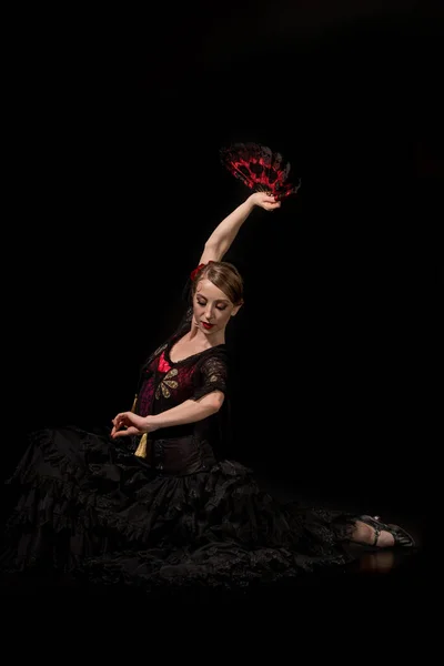Elegante Flamenco-Tänzerin hält Fächer über dem Kopf und sitzt auf schwarz — Stockfoto