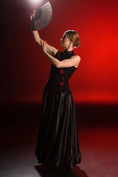 Pretty flamenco dancer in dress holding fan above head on red — Stock Photo