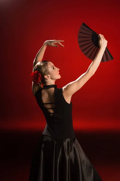 Joven bailarina flamenca en vestido mirando abanico sobre rojo - foto de stock
