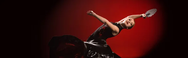 Tiro panorâmico do jovem dançarino de flamenco no vestido segurando fã enquanto dança no vermelho — Fotografia de Stock