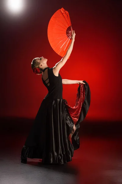Jeune femme en robe tenant ventilateur tout en dansant le flamenco sur rouge — Photo de stock