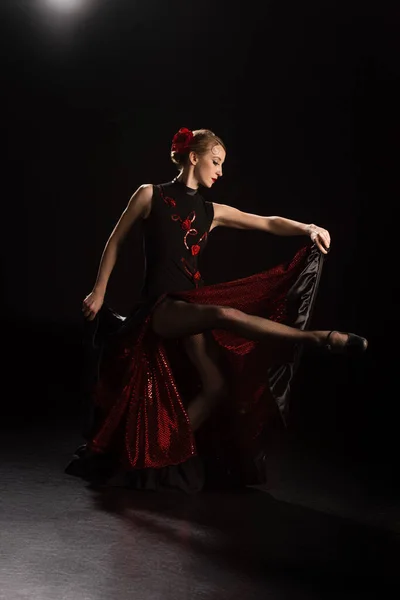 Side view of young woman touching dress and dancing flamenco on black — Stock Photo