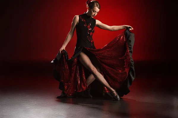 Mujer joven y hermosa tocando vestido mientras baila flamenco sobre rojo - foto de stock