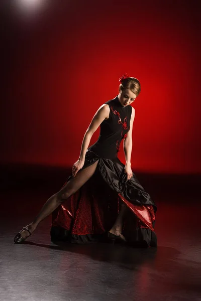 Young and attractive woman touching dress while dancing flamenco on red — Stock Photo