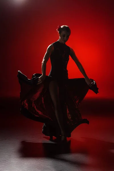 Silhouette of young woman touching dress and dancing flamenco on red — Stock Photo