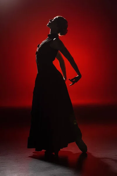 Silueta de elegante joven bailando flamenco sobre rojo - foto de stock