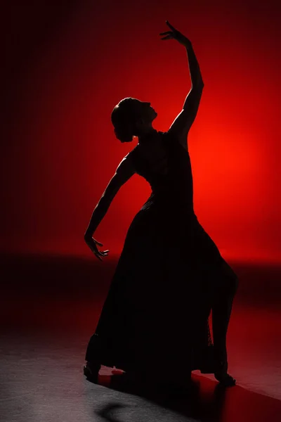 Silueta de niña elegante bailando flamenco sobre rojo - foto de stock