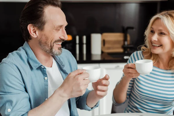 Belle femme souriante tenant une tasse de café près du mari dans la cuisine — Photo de stock