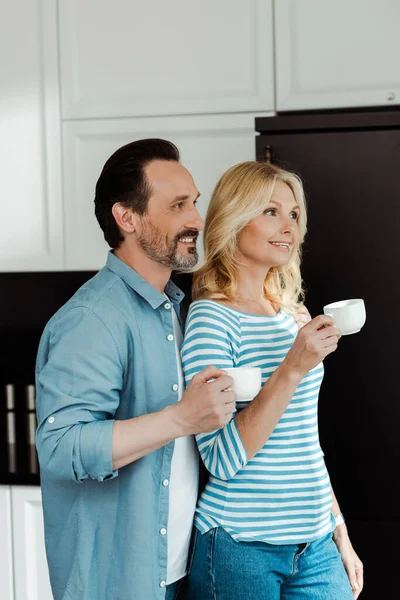 Sonriente pareja madura bebiendo café en la cocina - foto de stock