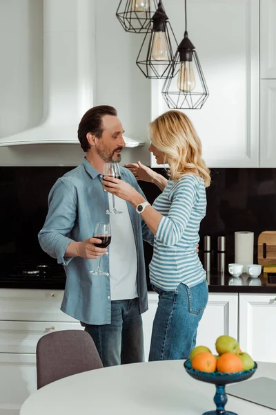 Selective focus of mature man embracing wife with glass of wine in kitchen — Stock Photo