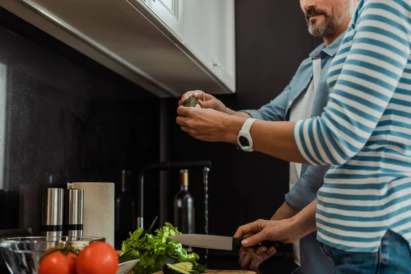 Vista ritagliata di coppia matura cucinare insalata fresca in cucina — Foto stock
