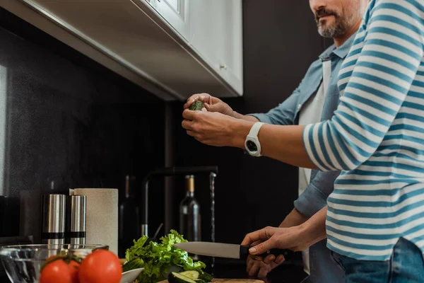 Vista recortada de pareja madura cocinando ensalada fresca en la cocina - foto de stock