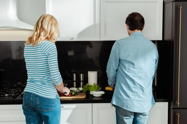 Vista posteriore di coppia cucinare insalata fresca sul piano di lavoro della cucina — Foto stock
