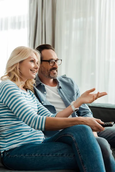 Smiling woman pointing with hand while watching tv with husband at home — Stock Photo